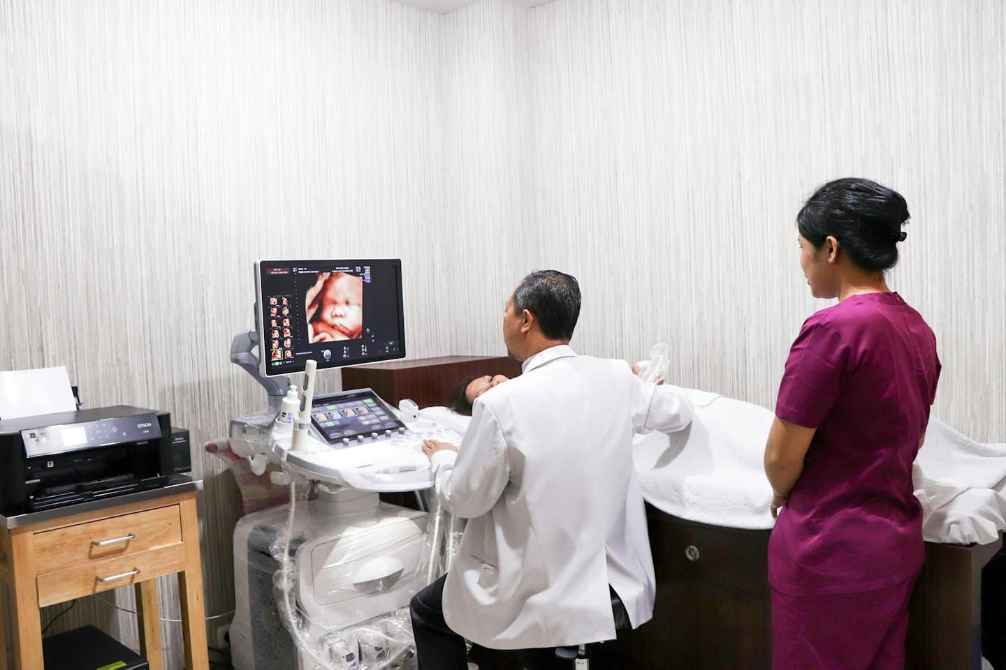 Medico esegue ecografia mostrando il viso del bambino a paziente e infermiera.